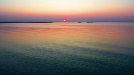 Start-of-Calm-Ocean-Sunrise-with-Dimmly-Lit-Sun-over-Small-Islands-on-the-Horizon
