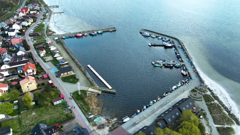 Aerial-view-of-Kuźnica-harbor-featuring-the-bustling-marina-with-moored-boats,-protective-sea-walls,-and-the-adjacent-village,-highlighting-the-integral-role-of-maritime-in-this-coastal-community