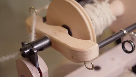 Close-up-hook-tool-pulls-grey-yarn-through-eye-in-spinning-wheel-spool
