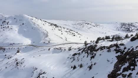Drone-view-of-car-passing-crossing-high-altitude-mountain-road-beautiful-slopes-covered-in-snow-winter-day