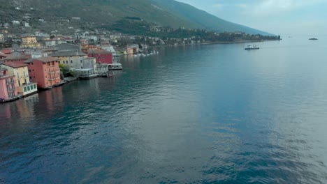 Cautivadoras-Imágenes-Aéreas-Capturan-La-Impresionante-Costa-Del-Lago-De-Garda,-Cerca-De-Malcesine,-Adornada-Con-Barcos-Y-Enmarcada-Por-Majestuosas-Montañas,-Ofreciendo-Un-Escenario-Pintoresco-Para-Los-Viajeros-Que-Exploran-Italia.