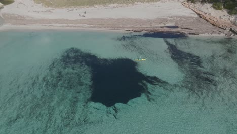 Geographical-formations-below-pristine-sea-water,-canoe-sailing-by-Aerial-Drone