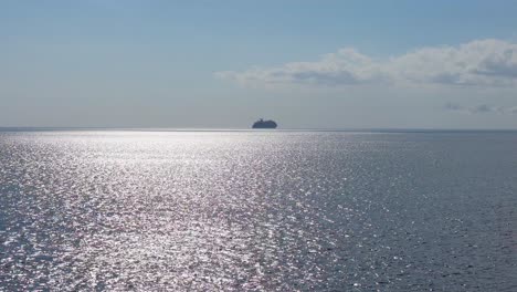 Aerial-trucking-pan-across-shimmering-ocean-water-with-cruise-ship-on-horizon-silhouette