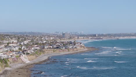 Wide-aerial-of-San-Diego-rocky-shore-and-cliffside-neighborhood-with-the-city-skyline-in-the-background-on-a-sunny-day