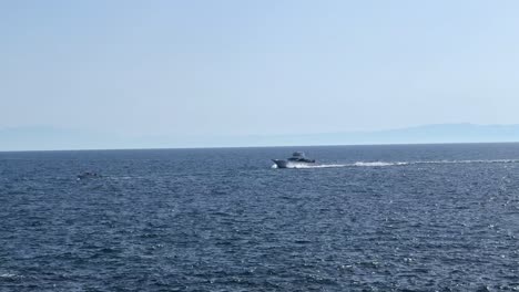 Boat-speeding-over-the-open-sea-with-distant-mountainous-coastline-on-a-clear-day
