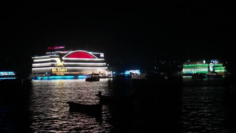 Night-view-of-colorful,-illuminated-casino-ships-floating-on-water-with-reflections,-calm-sea