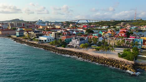 Aerial-dolly-above-Caribbean-sea-water-rises-to-orange-red-whtie-trimmed-roofs-of-Willemstad-Curacao
