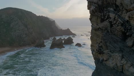 Toma-Aérea-De-Drones-De-La-Playa-De-Ursa-Con-Olas-Espumosas-Y-Rocas-Durante-La-Puesta-De-Sol-Dorada-En-Portugal