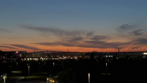 Die-Dämmerung-Senkt-Sich-über-Eine-Urbane-Skyline-Mit-Leuchtenden-Sonnenuntergangswolken-Und-Beginnenden-Lichtern-Der-Stadt