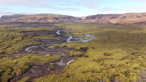A-meandering-river-through-iceland's-green-mossy-landscape,-light-sunshine,-aerial-view