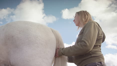 Upwards-angle-of-woman-stroking-tail-of-white-horse-during-horse-therapy