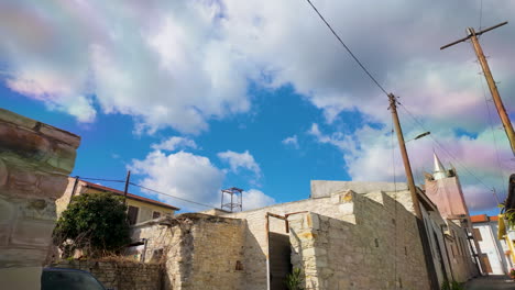 Vista-Del-Horizonte-De-Un-Pueblo-Chipriota-Dominado-Por-Nubes-Esponjosas-Contra-Un-Cielo-Azul-Profundo,-Mostrando-Antiguos-Edificios-De-Piedra-Y-Elementos-Modernos.
