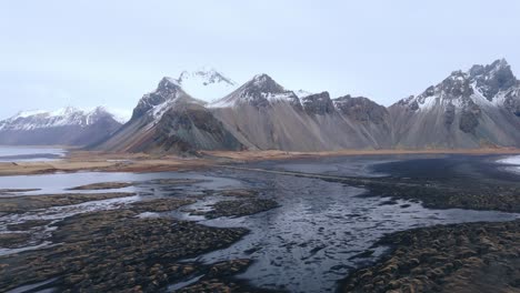 Black-sand-beach-at-low-tide-with-water-pools-below-mountain-range