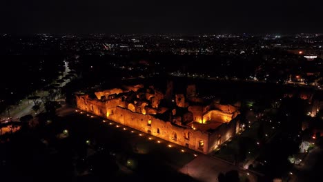 Una-Toma-Aérea-Revela-Los-Baños-De-Caracalla-Por-La-Noche-En-Roma,-Italia.