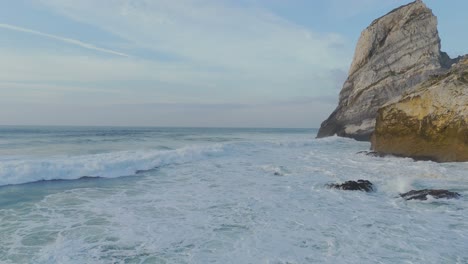 Aerial-drone-shot-of-Ursa-Beach-with-foamy-waves-and-boulder,-blue-sky-in-Portugal