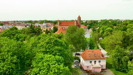 Closer-view-through-the-lush-tree-canopy-towards-the-castle-complex,-showcasing-the-historic-structure's-towering-presence-over-the-modern-and-traditional-buildings-of-the-town