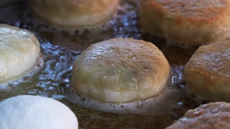 Night-market-food-vendor-drop-a-freshly-made-Chinese-meat-pie-on-hot-oil-pan,-close-up-shot-capturing-delicious-Xian-Bing-cooking-and-sizzling-on-the-pan,-popular-Asian-delicacy-cooking-in-process