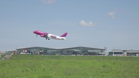 Pan-shot-of-Wizz-Air-plane-taking-off-toward-fleet-of-HSM-Global-delivery-vans