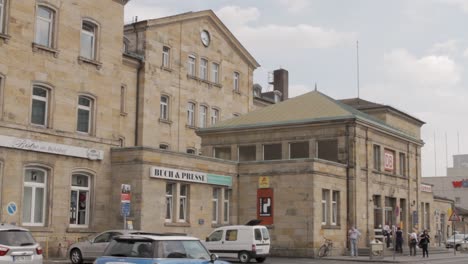 Historic-European-train-station-on-a-cloudy-day,-with-pedestrians-and-cars-outside