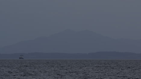 Hazy-blue-hour-layered-views-of-mountains-and-forest-peaks-in-distance-with-boat-on-water