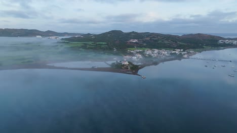 Menorca-Fornells-Bay-Village-establishing-aerial-shot-island-blue-sea-landscape-with-houses-and-green-mountain-background