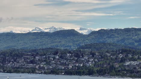 Left-moving-telephoto-drone-shot-of-the-distant-lake,-housing-and-alps-of-Switzerland-near-Zurich