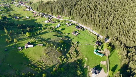 The-video-captures-aerial-footage-of-Slatioara-village-in-Romania,-showcasing-its-simple-houses,-a-winding-road,-and-the-village-nestled-amidst-hills-covered-with-trees