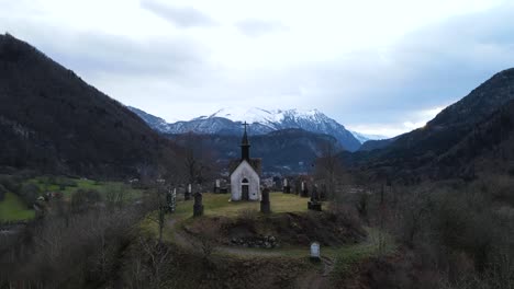 Mysteriös-Aussehende-Aufnahme-Einer-Kapelle-Auf-Einem-Hügel,-Umgeben-Von-Einem-Kreis-Aus-Grabsteinen-Und-Bergen