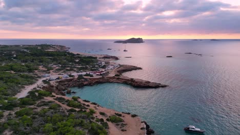 Cielo-Rosa-Púrpura-Playa-De-Cala-Comte-Con-Barcos,-Impresionante-Cielo-Al-Atardecer-En-Ibiza