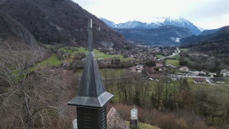 Cruz-De-La-Iglesia-Sobre-El-Valle-Con-El-Amanecer-Y-Un-Pequeño-Pueblo-En-El-Valle-De-Montaña-Al-Fondo.