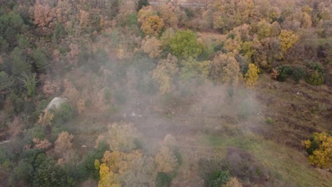 Osona's-foggy-landscape-in-autumn,-showcasing-colorful-trees-and-rocky-terrain,-aerial-view