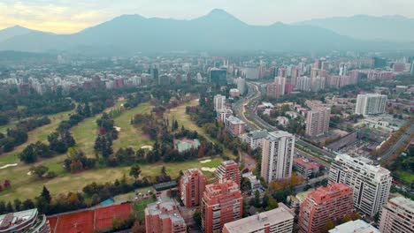Bird's-eye-view-establishing-in-El-Golf-neighborhood-with-Manquehue-hill,-cloudy-day,-golf-course,-wealthy-area-of-Santiago-Chile