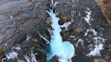 The-stunning-bruarfoss-waterfall-in-iceland,-showcasing-its-vibrant-blue-waters-and-rocky-surroundings,-aerial-view