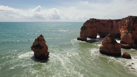 Zwei-Natürliche-Bögen-Mit-Felsnadeln-Und-Brechenden-Wellen,-Luftaufnahme-Aus-Der-4K-Drohne-Mit-Umgekehrtem-Schwenk-Nach-Unten-Auf-Den-Malerischen-Strand-Estrada-Da-Caramujeira-In-Der-Algarve-Region-Von-Portugal