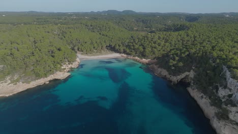 Luftdrohne-Fliegt-über-Große-Waldlandschaft-Mit-Blauer-Meeresbucht,-Natürlicher-Menorca-Spanienumgebung,-Cala-Mitjana