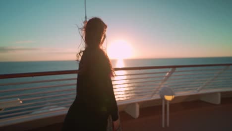 Woman-in-a-dress-walking-on-the-deck-of-a-cruise-in-the-evening,-feeling-wind-and-looking-out-to-sea-sunset