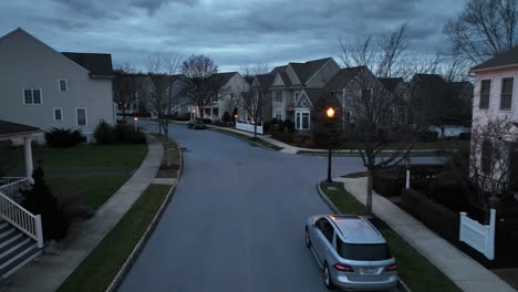 Twilight-scene-in-a-suburban-neighborhood-featuring-well-lit-homes-with-porches,-neat-lawns,-and-a-car-parked-on-street