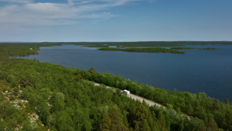 Aerial-view-following-a-camper-driving-in-front-of-the-Inarinjarvi-lake-in-Finland