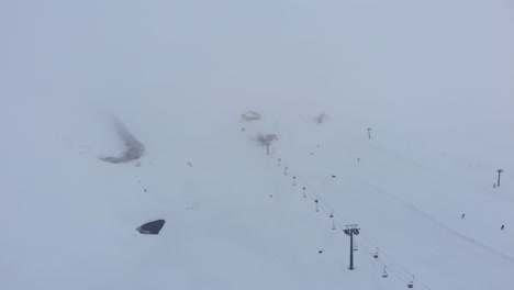 Aerial-foggy-winter-snow-covered-ski-resort-with-very-few-people-moody-winter-day