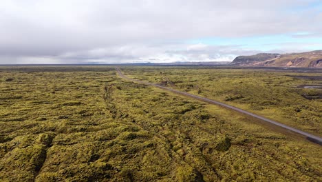 A-vast-moss-covered-lava-field-in-iceland-with-an-open-road,-aerial-view