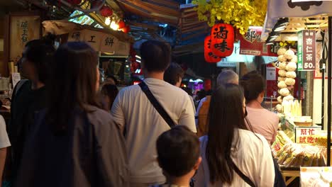 Visitors-leisurely-stroll-along-a-quaint-alleyway-adorned-with-food-vendors-and-souvenir-shops-in-Jiufen-Old-Street,-a-renowned-tourist-destination-nestled-within-Taiwan's-mountainous-terrain