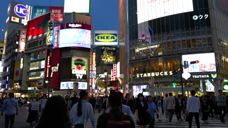 POV-walking-across-Shibuya-crossing-at-night,-looking-up-to-adverts