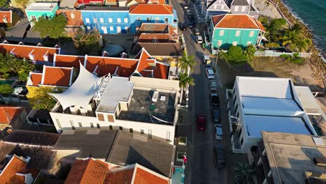 Orange-roofs-and-blue-green-buildings-along-Caribbean-coastline-in-Willemstad-Curacao,-city-establishing-at-sunset