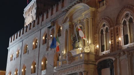 Bolonia,-Italia-Y-Banderas-De-La-UE-Ondeando-En-La-Fachada-Del-Palacio-De-Accursio-Por-La-Noche-Con-La-Estatua-Del-Papa-Gregorio-XIII-Disfrazado-De-San-Petronio