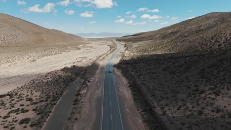 Aerial-view-of-vehicles-traveling-on-extensive-paved-road-in-arid-landscape-of-Jujuy,-Argentina