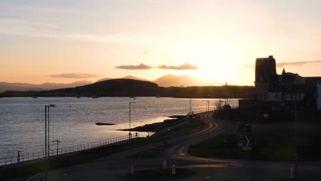 Atardecer-Dorado-Escocés-Con-Rayos-De-Luz-Sobre-La-Tranquila-Y-Plácida-Bahía-De-Oban-Con-Siluetas-De-Edificios-Y-Océano-En-El-Oeste-De-Escocia,-Reino-Unido