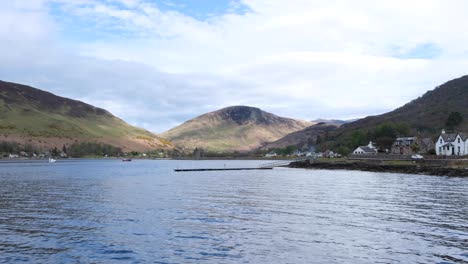 Scenic-landscape-view-from-passenger-ferry-of-the-Isle-of-Arran-with-water,-mountains-and-the-village-of-Lochranza-in-Western-Scotland-UK