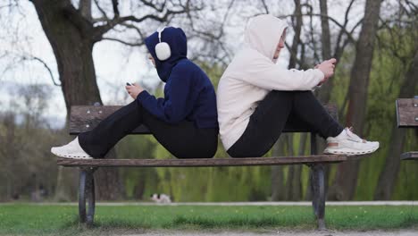 Distracted-couple-with-smartphones-sit-on-outdoor-wooden-bench-with-their-backs