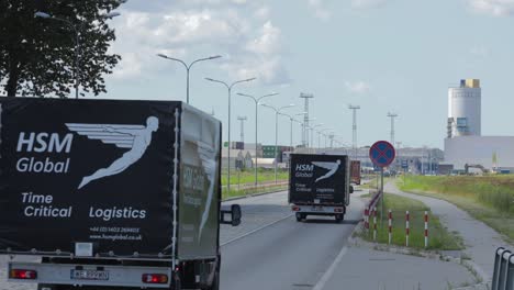 Fleet-of-HSM-Global-delivery-vans-drive-by-on-road-on-city-outskirts,-static