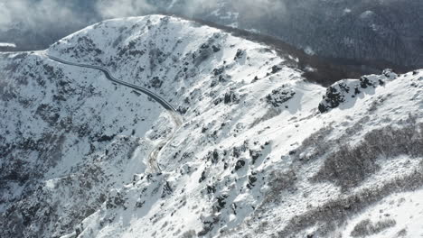 Winding-road-cuts-through-a-snowy-mountain-landscape,-aerial-view